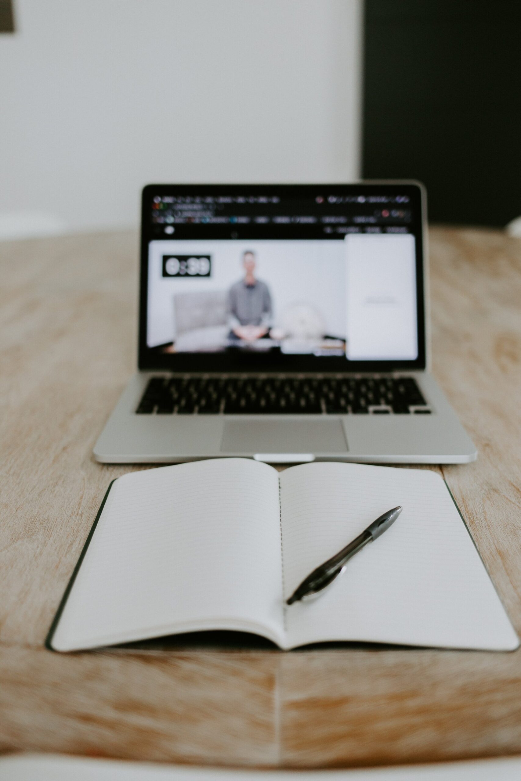 A laptop streaming an online trading course and a pen on an open note