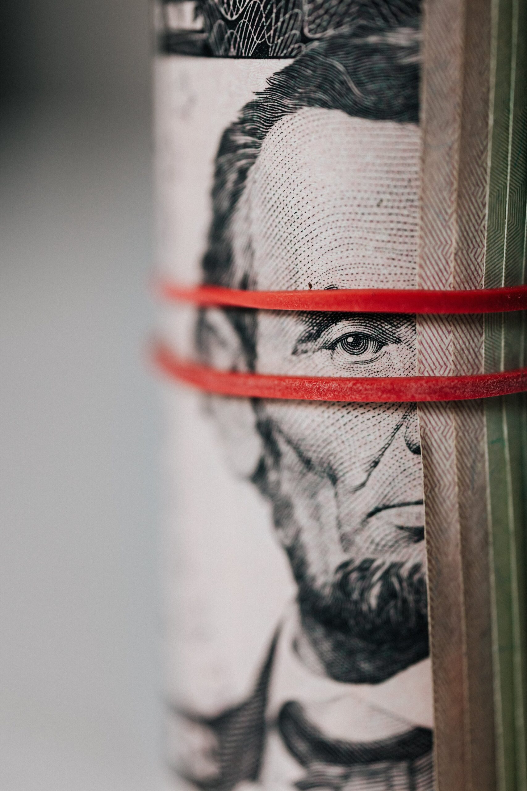 A 5 dollar bill strapped with a rubber band, showing Abraham Lincoln's face. Depicting Greed